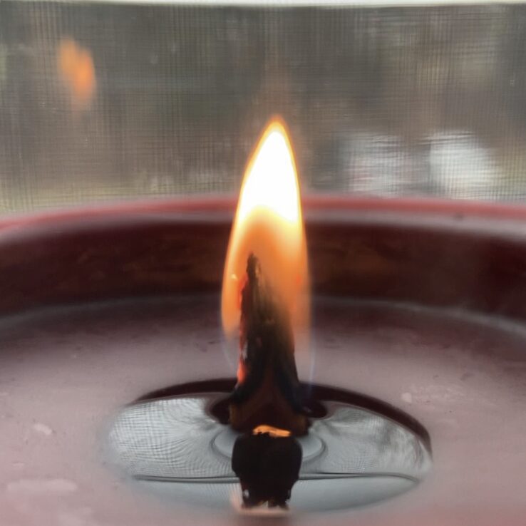 Close up of a red candle burning with a pool of dark red wax.